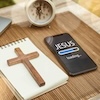 Das-Bild-zeigt-einen-leeren-Block-auf-welchem-ein-braunes-holzkreuz-liegt-daneben-liegt-ein-iphone-auf-dem-tisch-welches-auf-dem-display-jesus-zeigt-und-darunter-einen-ladebalken-mit-loading